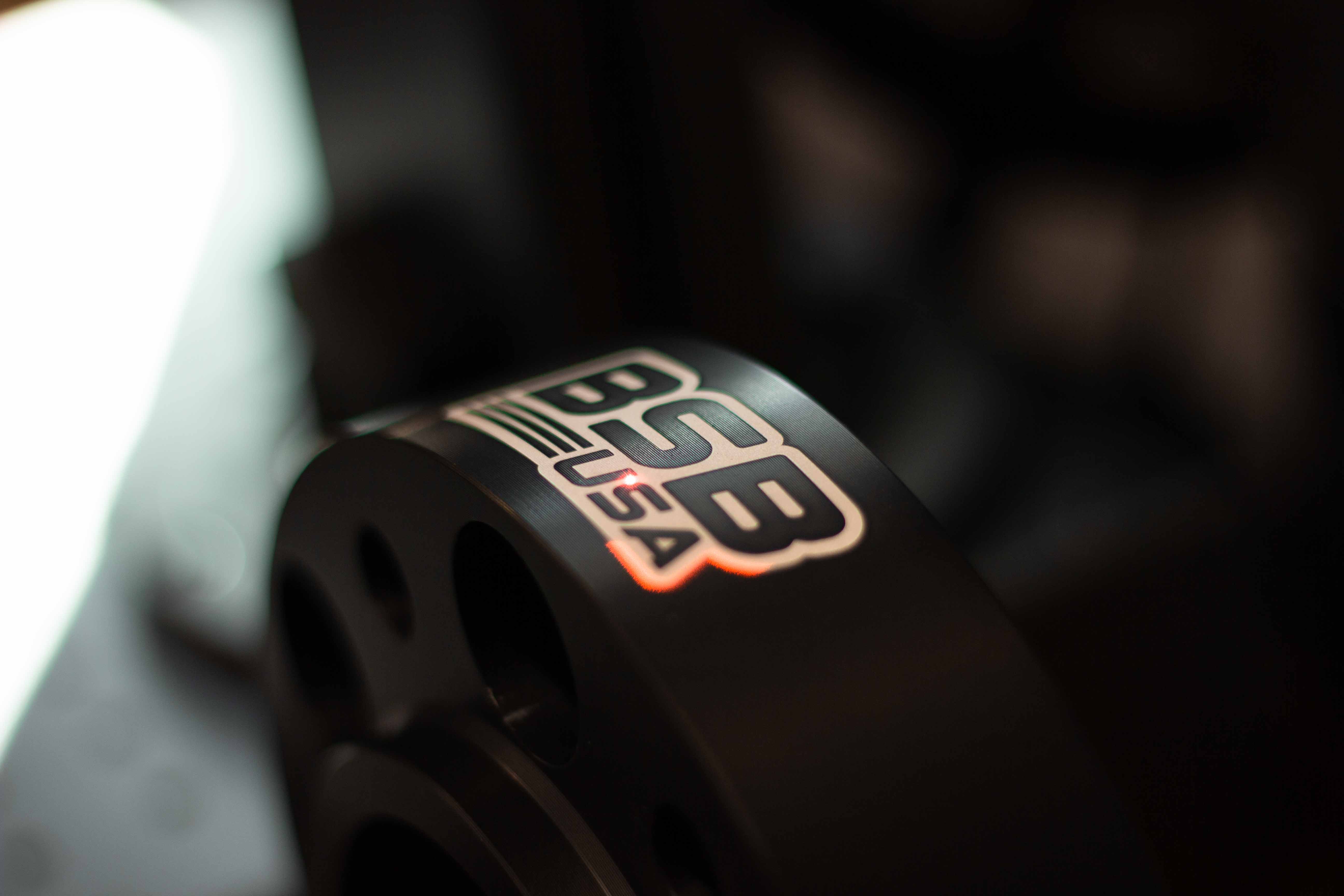 Close-up of a black anodized wheel spacers being laser engraved with the BSB USA logo.